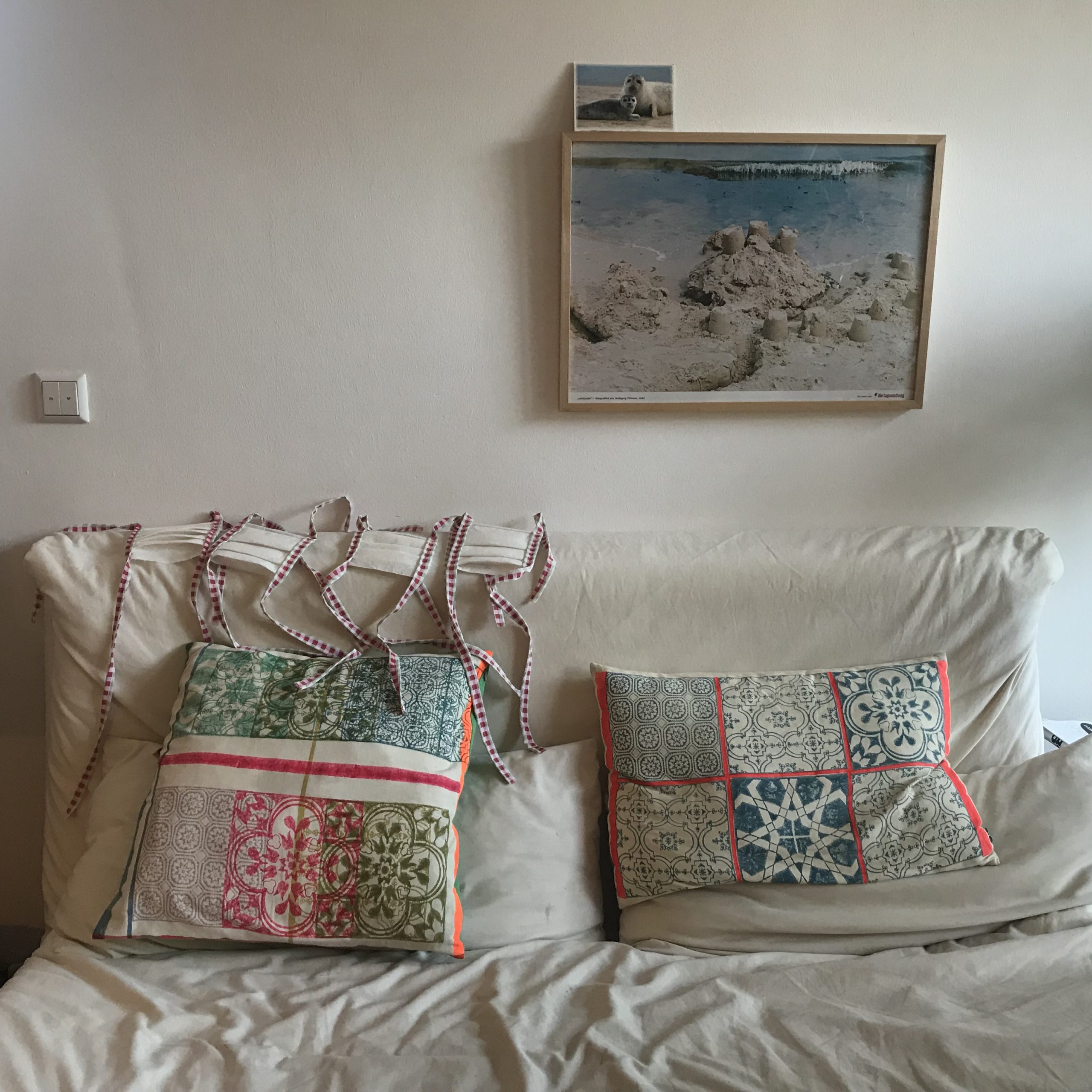 Sofa mit Bild darüber und zwei Kissen. Auf dem Sofa legen 4 Mundschutze